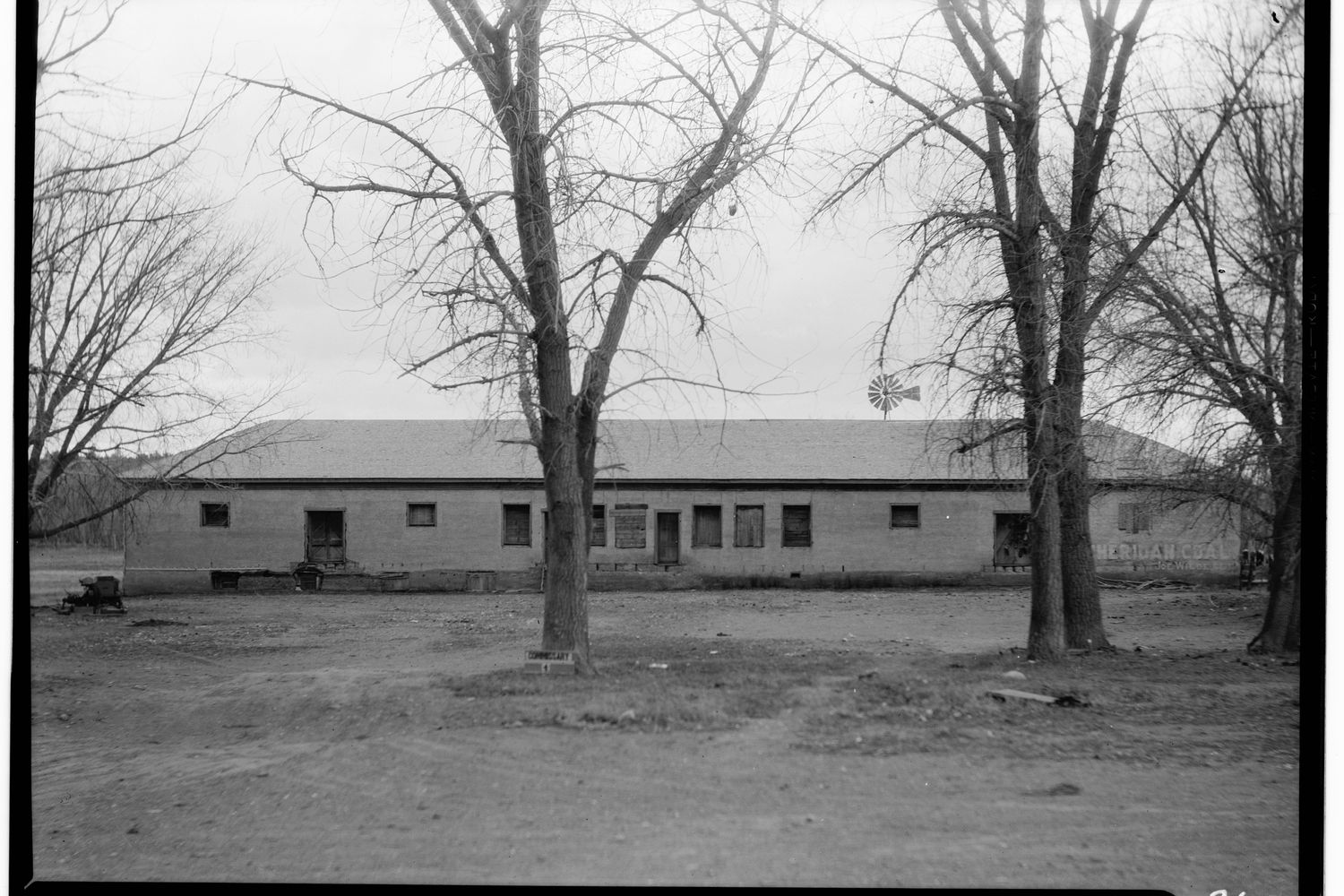 The long low commissary storehouse at Fort Laramie behind bare cottonwoods in a survey photograph.